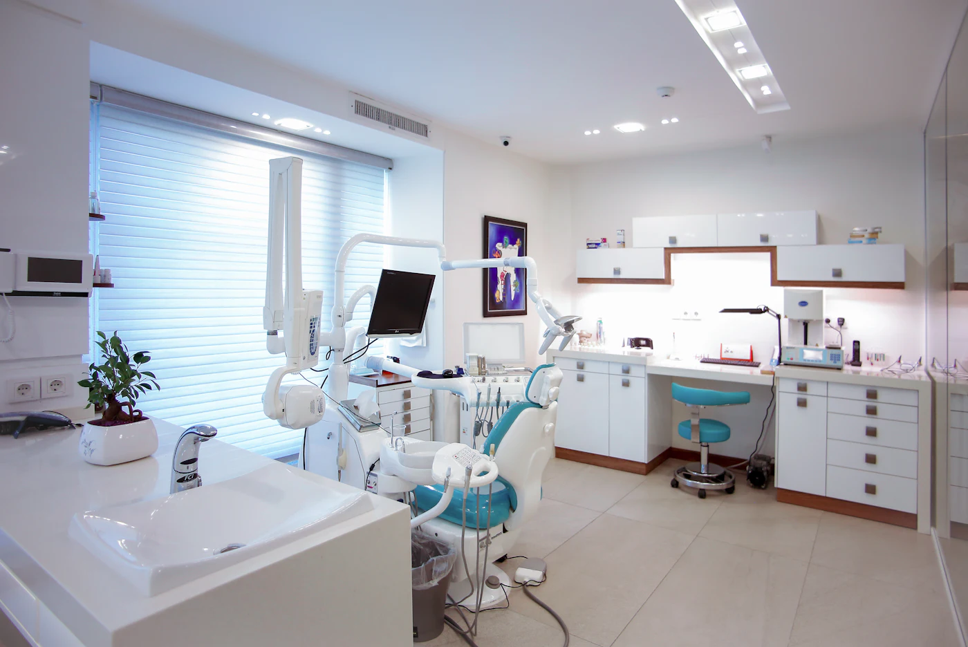 A bright dental treatment room with a white and turquoise chair.